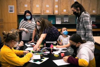 Four middle school girls work on creating paper models of shapes like pyramids, cubes and dodecahedrons with the help of Dr. Margaret Watts and Dr. Barbara Jennings Herzog, who teach math at Doane University, and Bailee Baack, a junior elementary and special education major. They are in one of the classrooms in Doane's Lied science building. 